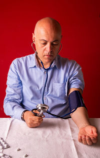 Mid adult man sitting on table against red background