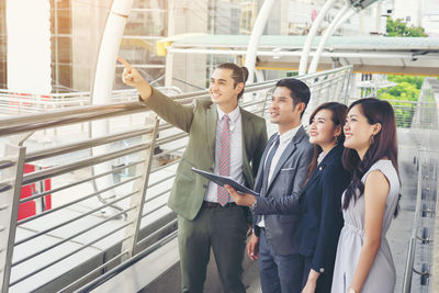 Smiling businessman showing something to colleagues standing on elevated walkway 