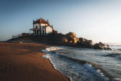 Lighthouse by sea against sky during sunset