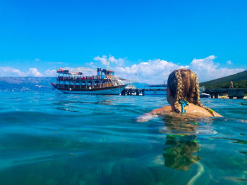 Rear view of woman swimming in sea against sky during sunny day