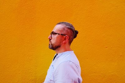 Side view of man standing against yellow wall