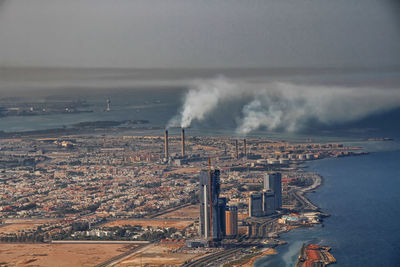 Smock stacks emitting smoke at coastline against sky