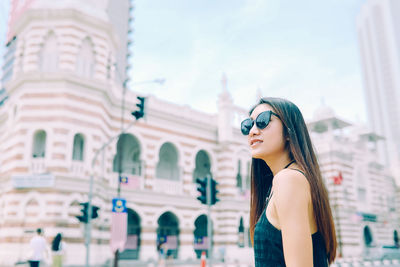 Young woman wearing sunglasses standing against historic building