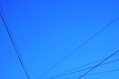 Low angle view of power cables against clear blue sky