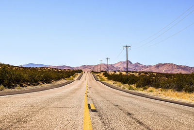 Road leading towards mountain against clear sky