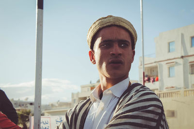 Portrait of young man standing against sky in city