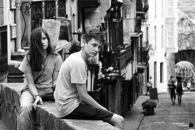 Portrait of couple sitting on retaining wall in city