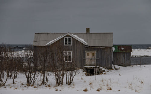 Abandoned house on snow covered field against sky