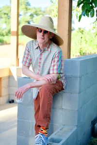 Portrait of smiling senior man wearing straw hat while standing against retaining wall