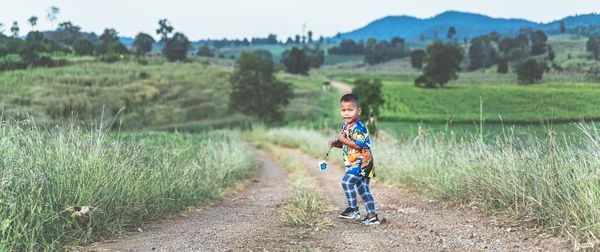 Full length of boy standing on dirt road at rural area against field
