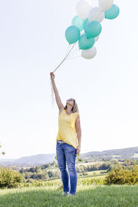 Full length of woman holding balloons against clear sky