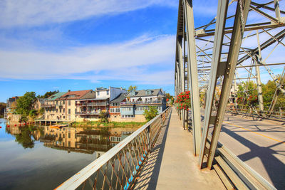 Footbridge over river amidst buildings against sky