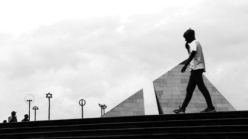 Side view of man standing on railing against sky