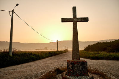 Cross on field by road against sky during sunset