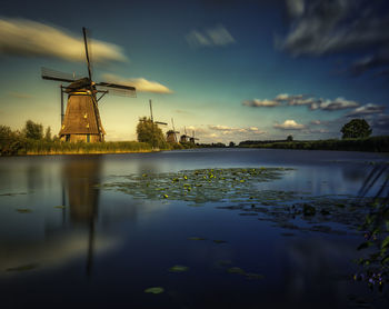 Scenic view of windmills by lake against sky