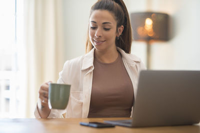 Young woman with coffee cup sitting at table