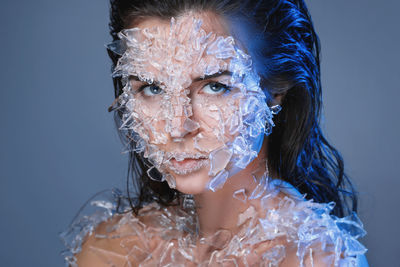 Portrait of woman with broken glass on body against purple background