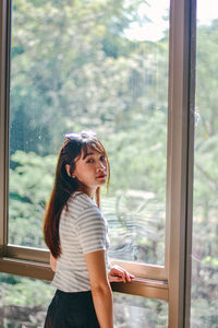Portrait of young woman standing by window at home