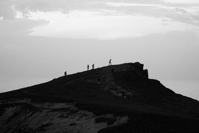 Silhouette people on rock against sky