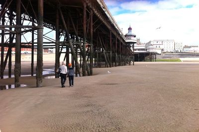 Rear view of mother and son walking by pier at beach against sky