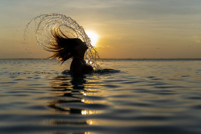 Silhouette woman in sea against sky during sunset