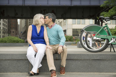 Mature couple kissing while sitting on steps in city