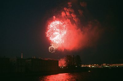 Firework display over illuminated city against sky at night