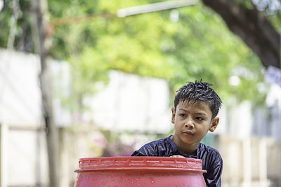 Boy looking away by wet barrel against trees