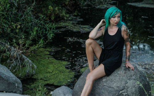 Punk woman sitting on rock against pond