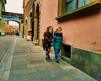 Siblings walking on footpath in city