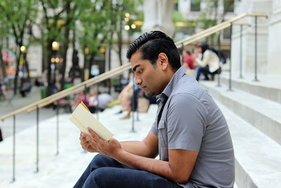 Young man sitting on mobile phone in city