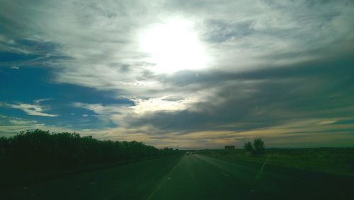 Road passing through field against cloudy sky