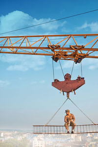 Low angle view of crane against bridge against sky