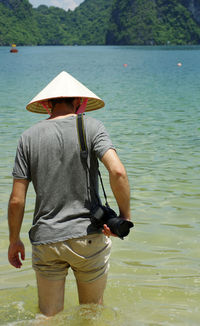 Rear view of man with camera walking in sea
