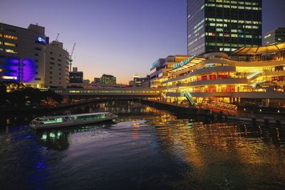 Illuminated bridge over river by buildings in city at night