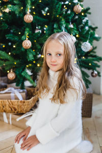 Portrait of smiling girl sitting by christmas tree at home