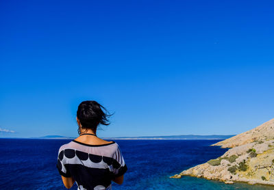 Rear view of woman standing by sea against clear blue sky