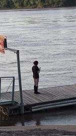 Rear view of man standing on pier over lake