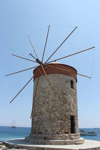 Traditional windmill by sea against clear sky