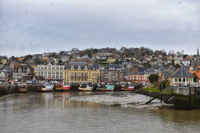 Sailboats moored on river by buildings in city against sky