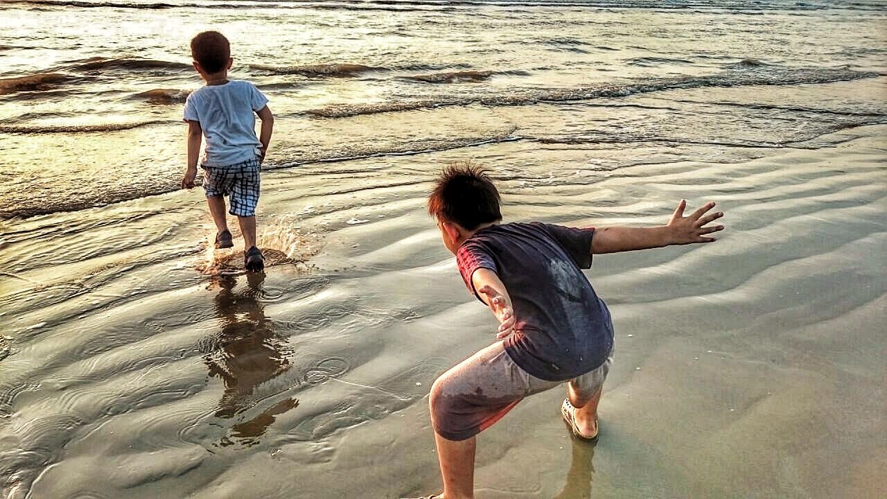 REAR VIEW OF SIBLINGS AT BEACH