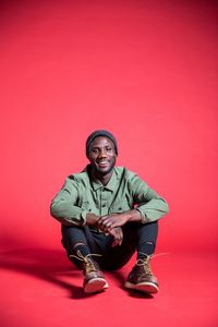 Portrait of young man sitting against red background