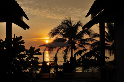 Silhouette palm trees by swimming pool against sky during sunset