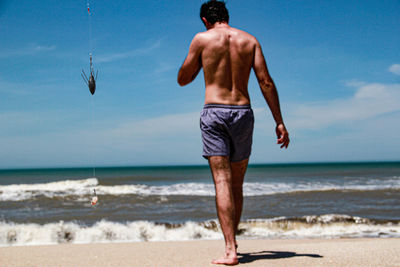 Rear view of shirtless man walking on beach