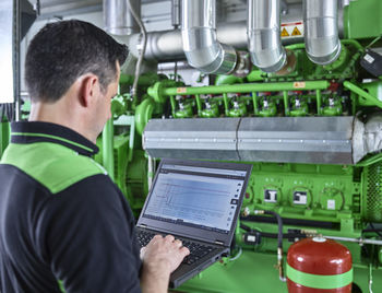 Combined heat and power plant, worker using laptop in front of gas engine