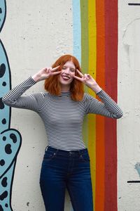 Smiling young woman gesturing while standing against wall