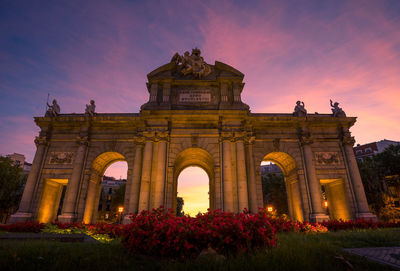 From below of illuminated alcala gate located in madrid against amazing sunset sky