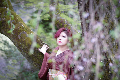 Portrait of young woman in kimono standing against tree