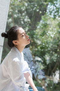 Young woman looking away against trees