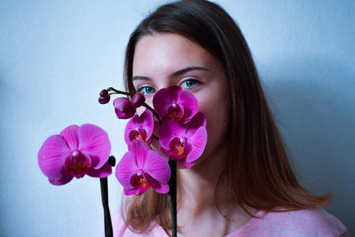 Close-up portrait of woman with pink orchids against blue wall